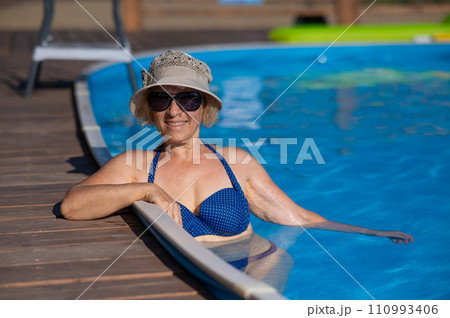 An elderly woman in a hat and sunglasses swims in the pool. Retirement leave. An elderly woman in a hat and sunglasses swims in the pool. Retirement leave. 110993406