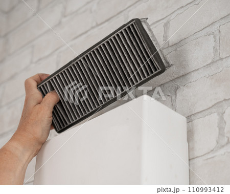A man changes the filter at the supply ventilation. Gadget for ventilation, disinfection and air purification of the apartment. A man changes the filter at the supply ventilation. Gadget for ventilation, disinfection and air purification of the apartment. 110993412