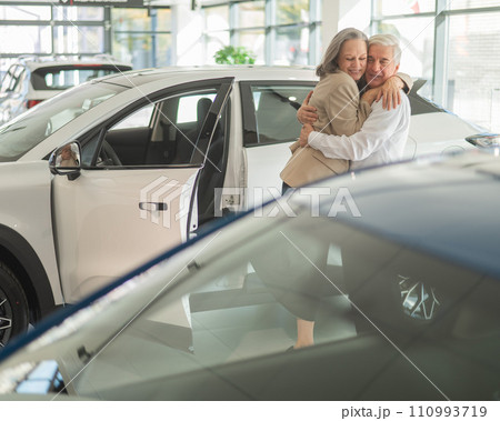 Mature Caucasian couple hugging. Elderly man and woman buying a new car. Mature Caucasian couple hugging. Elderly man and woman buying a new car. 110993719