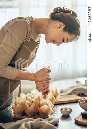 young woman applies cream to cupcakes in craft paper. the concept of food delivery. a birthday package. small business. bakery chef bakes cakes in kitchen 110993954