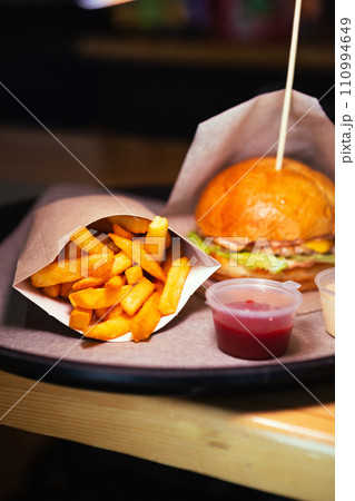 Side view of fresh cheeseburger with chicken and fries with red sauce on wooden table. High quality photo. Selective focus. Unhealthy eating concept 110994649