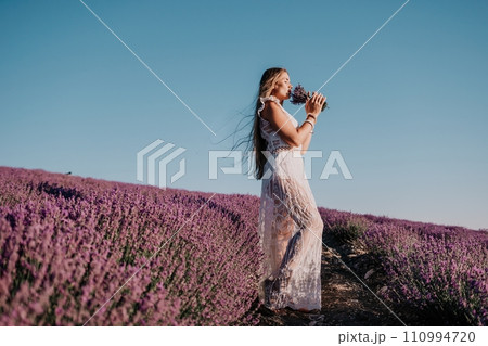 Woman lavender field. Happy carefree woman in a white dress walking in a lavender field and smelling a lavender bouquet on sunset. Ideal for warm and inspirational concepts in wanderlust and travel. Woman lavender field. Happy carefree woman in a white dress walking in a lavender field and smelling a lavender bouquet on sunset. Ideal for warm and inspirational concepts in wanderlust and travel. 110994720