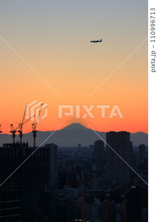 View of Mt. Fuji as seen from central Tokyo at sunset with a plane flying above in the orange sky View of Mt. Fuji as seen from central Tokyo at sunset with a plane flying above in the orange sky 110996713