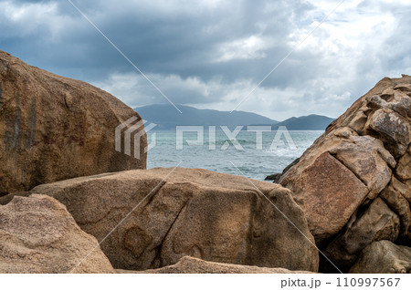 Coastal waves crash against monumental granite boulders lining shore. majestic seascape features vast expanse of rocks, under turbulent, cloud-laden sky, untamed natural panorama Coastal waves crash against monumental granite boulders lining shore. majestic seascape features vast expanse of rocks, under turbulent, cloud-laden sky, untamed natural panorama 110997567