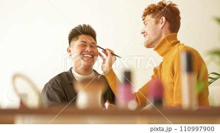 Cosmetic on a shelf while gay couple applying make up 110997900