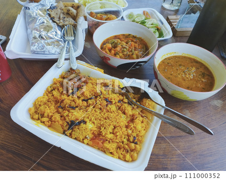 A variety of Indian dishes like dal bhat, veg dum biryani, roti and chhole or chickpea curry served in takeout containers on a wooden table A variety of Indian dishes like dal bhat, veg dum biryani, roti and chhole or chickpea curry served in takeout containers on a wooden table 111000352
