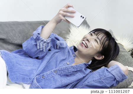 ソファに寝転んでスマホ動画を観る女性 ソファに寝転んでスマホ動画を観る女性 111001207