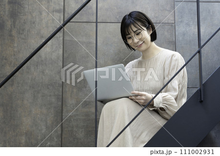 階段でノートパソコンを使う眼鏡の女性 111002931