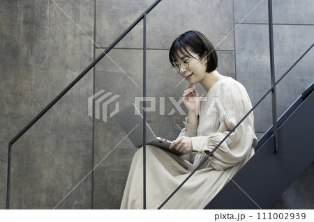 階段でノートパソコンを使う眼鏡の女性 111002939