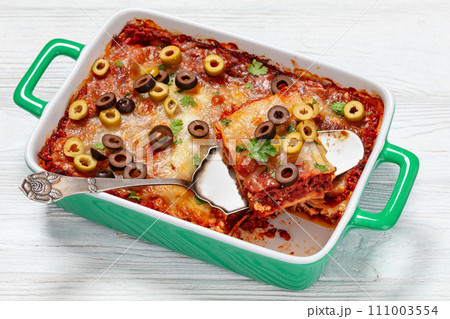 lasagna with olive rings in green baking dish 111003554