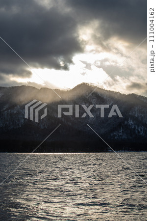 雲に遮られた夕陽の光が山に射す山間の湖のドラマチックな風景。北海道の屈斜路湖。 111004162