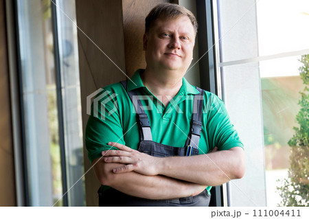 Portrait of a tired worker in overalls sitting by the window Portrait of a tired worker in overalls sitting by the window 111004411