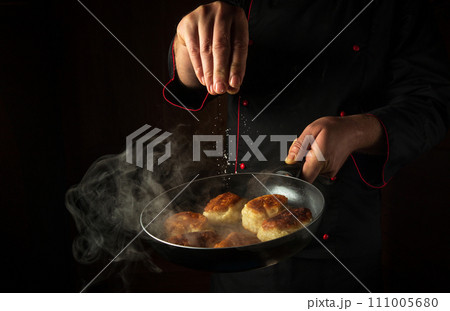 The cook adds salt to oladki in a frying pan. The concept of preparing a delicious Ukrainian national dish or bliny in the kitchen. Black space for advertising The cook adds salt to oladki in a frying pan. The concept of preparing a delicious Ukrainian national dish or bliny in the kitchen. Black space for advertising 111005680