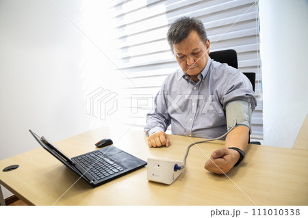 Asian man in 50s checking blood pressure with instrument in the work office 111010338