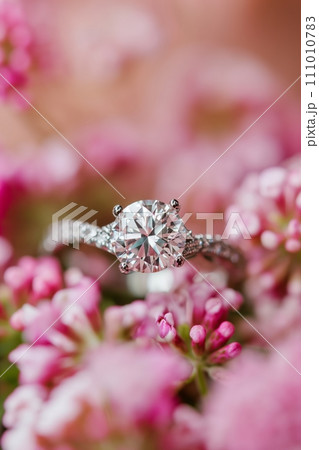 Diamond engagement ring on a pink floral background. Luxury female jewelry close up 111010783