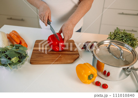 Woman cutting bell pepper. Happy smiling cute female is preparing a fresh healthy vegan salad with many vegetables in the kitchen at home and trying a new recipe 111010840