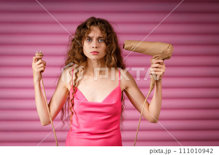 Young positive smiling woman receives surprise gift hand hold hair dryer wrapped in rustic beige craft paper. Black Friday concept on pink background. Young positive smiling woman receives surprise gift hand hold hair dryer wrapped in rustic beige craft paper. Black Friday concept on pink background. 111010942