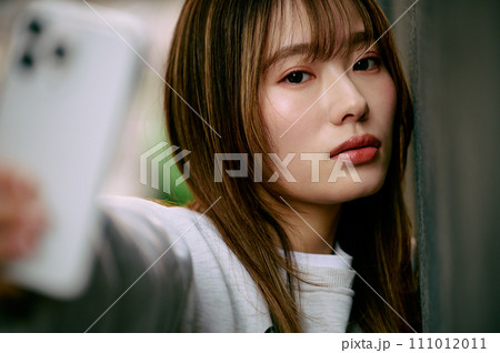 壁に寄りかかって自撮りする若い女性 111012011