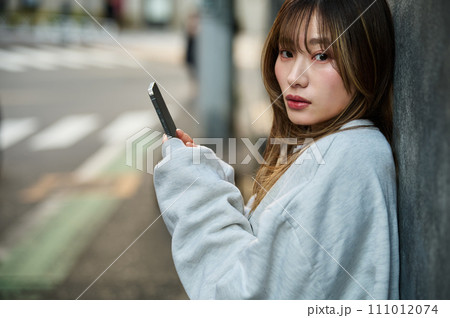 壁に寄りかかってスマホを操作する若い女性 壁に寄りかかってスマホを操作する若い女性 111012074