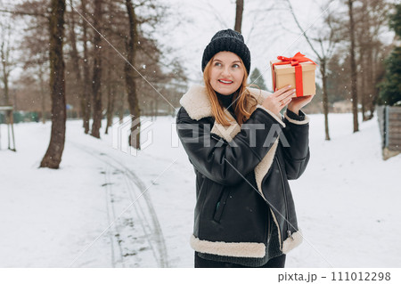 Cheerful blonde girl holding gift boxes on the park background. 30s female relaxing outdoors, winter time. Sale, shopping, holidays banner 111012298