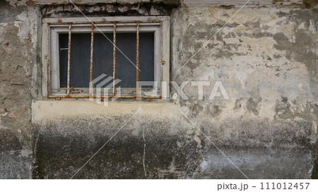 lattice window on a shabby dirty wall as a rough gloomy texture background, part of the wall of a terrible building with a window with iron bars, window to a basement or prison cell 111012457