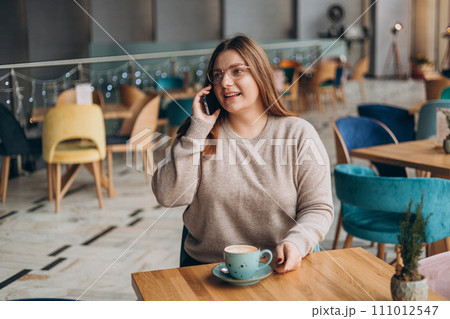 Attractive 30s female with cup of coffee having talking conversation with mobile phone while rest in cafe. Casual young woman using mobile phone indoors Attractive 30s female with cup of coffee having talking conversation with mobile phone while rest in cafe. Casual young woman using mobile phone indoors 111012547