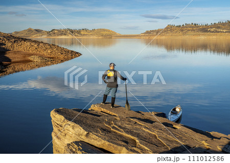 male canoe paddler with a paddle on  a rocky shore of a mountain lake - Horsetooth Reservoir in northern Colorado in fall or winter scenery 111012586