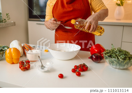 Female chef in a uniform pours olive oil from a bottle. Caucasian female food blogger working explaining how to cook a dish Female chef in a uniform pours olive oil from a bottle. Caucasian female food blogger working explaining how to cook a dish 111013114