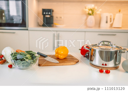 Different fresh vegetables on white table in modern kitchen. Products and blurred view of kitchen interior on background 111013120