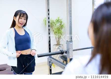 プライベートジムの鏡で体をチェックする若い女性　パーソナルジム　筋トレ女子　個室 111014459