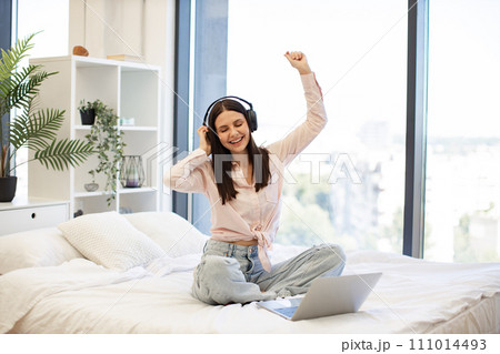 Woman relaxing on bed at home and using headphones for listening songs. Woman relaxing on bed at home and using headphones for listening songs. 111014493