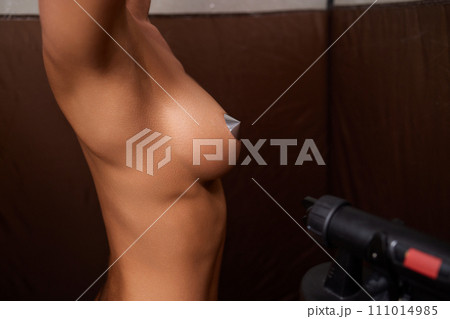 Cosmetologist using airbrush for spray tan apply to young woman body in beauty salon. Cosmetologist using airbrush for spray tan apply to young woman body in beauty salon. 111014985