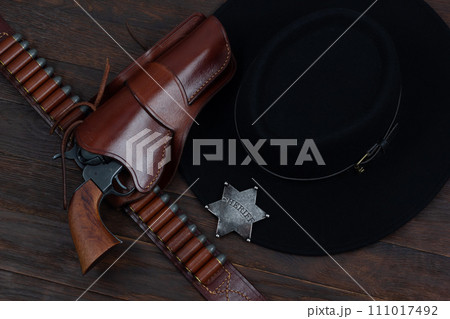 Sheriff star with gun, holster and gun belt with old west hat on table. Top view. 111017492