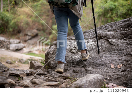 Close-up legs image of a woman is hiking with a trekking pole on the rock mountain. Close-up legs image of a woman is hiking with a trekking pole on the rock mountain. 111020948