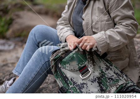A woman finding something in her backpack while taking a break during her hiking trip. A woman finding something in her backpack while taking a break during her hiking trip. 111020954