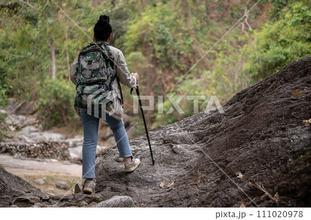 An adventure Asian woman with a backpack and a trekking pole is hiking on a rock mountain alone. 111020978
