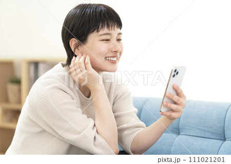 ソファーに座りスマートフォンを使う若い女性 111021201