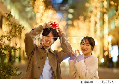 プレゼントを手にする男女とイルミネーションが輝く街並み 111021251