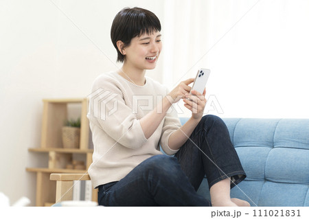 ソファーに座りスマートフォンを使う若い女性 111021831