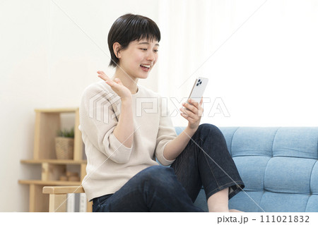 ソファーに座りスマートフォンを使う若い女性 111021832