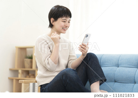 ソファーに座りスマートフォンを使う若い女性 111021833