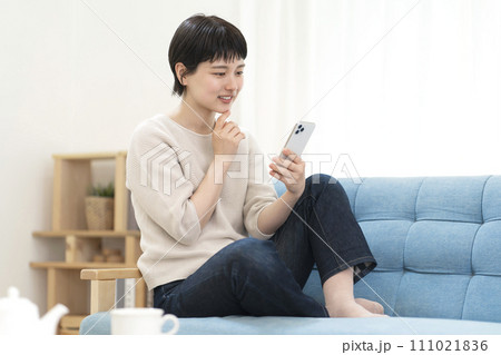 ソファーに座りスマートフォンを使う若い女性 111021836