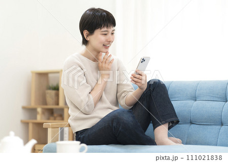 ソファーに座りスマートフォンを使う若い女性 ソファーに座りスマートフォンを使う若い女性 111021838