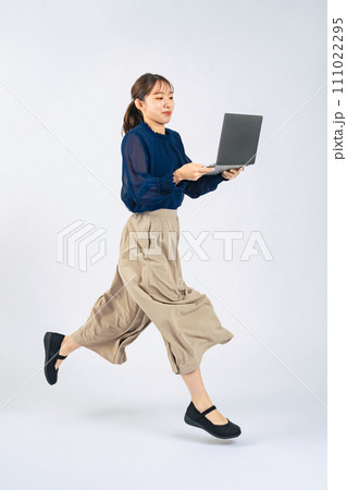 ノートパソコンを持ってジャンプするカジュアルウェアを着た女性 ノートパソコンを持ってジャンプするカジュアルウェアを着た女性 111022295