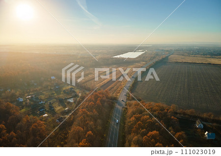 Aerial view of intercity road with fast driving cars between autumn forest trees at sunset. Top view from drone of highway traffic in evening 111023019