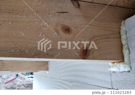 Installation of wooden beams of roof frame with spray foam on a house wall under construction. 111023265