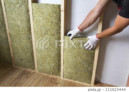 Close-up of worker hands in white gloves insulating rock wool insulation staff in wooden frame for future walls for cold barrier. Comfortable warm home, economy, construction and renovation concept. 111023444