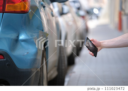 Driver hand photographing on sellphone camera dented vehicle on street side for insurance service after car accident. Road safety concept 111023472