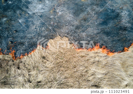 Aerial view of grassland field burning with red fire during dry season. Natural disaster and climate change concept Aerial view of grassland field burning with red fire during dry season. Natural disaster and climate change concept 111023491