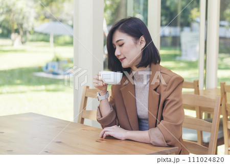 Beauty woman drinking black coffee in coffee shop holding freshness cup. Coffee lover. Asian Woman drink black coffee hand holding cup at green garden cafe. Young woman smile face love drink coffee Beauty woman drinking black coffee in coffee shop holding freshness cup. Coffee lover. Asian Woman drink black coffee hand holding cup at green garden cafe. Young woman smile face love drink coffee 111024820
